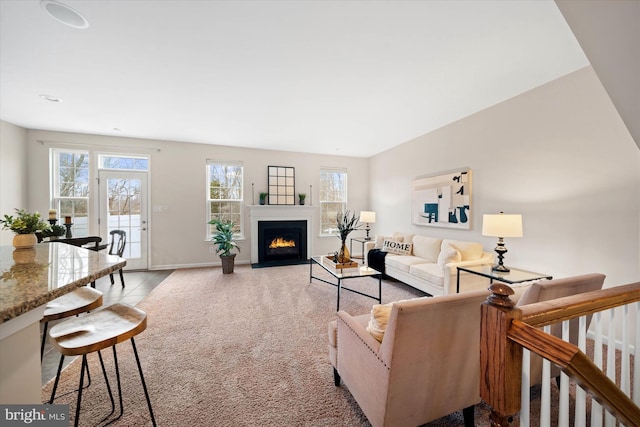 living room with a fireplace with flush hearth, a wealth of natural light, light colored carpet, and baseboards