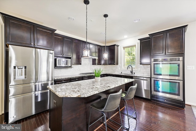 kitchen with stainless steel appliances, a sink, dark brown cabinetry, and light stone countertops