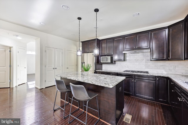 kitchen featuring dark wood-style floors, appliances with stainless steel finishes, a kitchen island, under cabinet range hood, and a kitchen bar