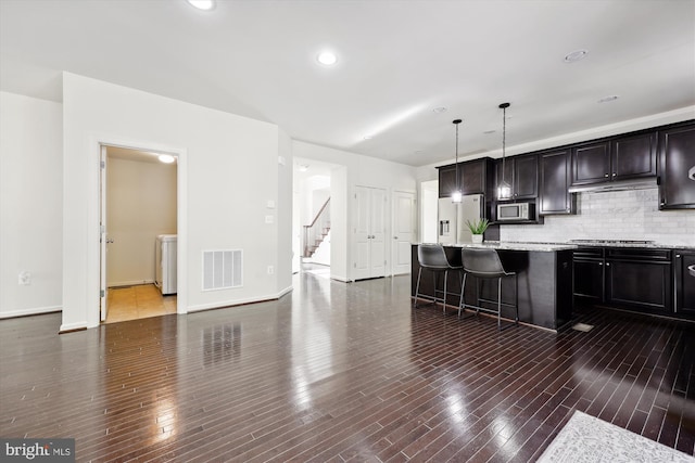 kitchen with stainless steel appliances, a breakfast bar, dark wood-type flooring, visible vents, and decorative backsplash