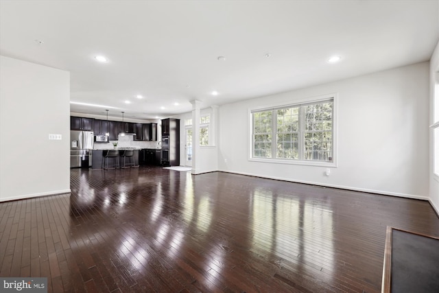 living room featuring dark wood-type flooring, recessed lighting, ornate columns, and baseboards