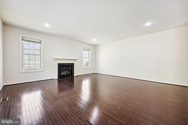 unfurnished living room with dark wood-type flooring, recessed lighting, baseboards, and a fireplace with flush hearth