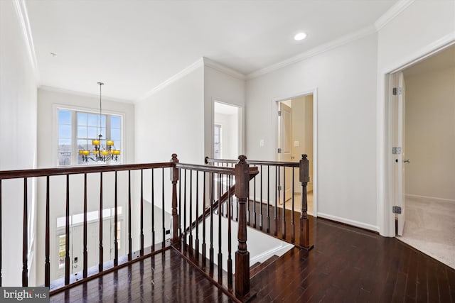 hall featuring baseboards, wood finished floors, an inviting chandelier, crown molding, and an upstairs landing