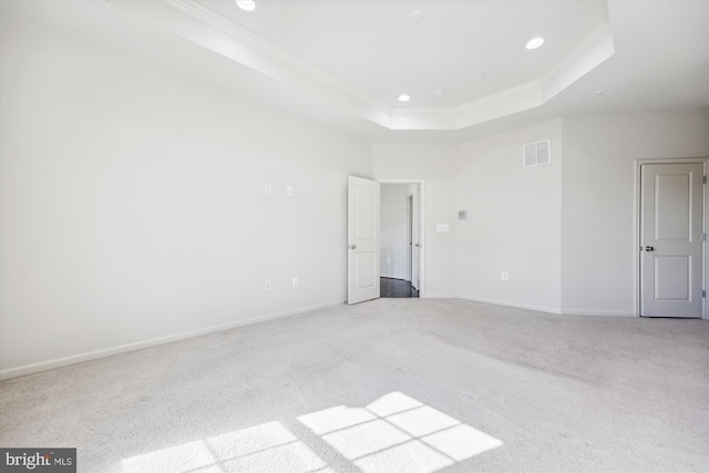 empty room with carpet flooring, visible vents, baseboards, a raised ceiling, and crown molding