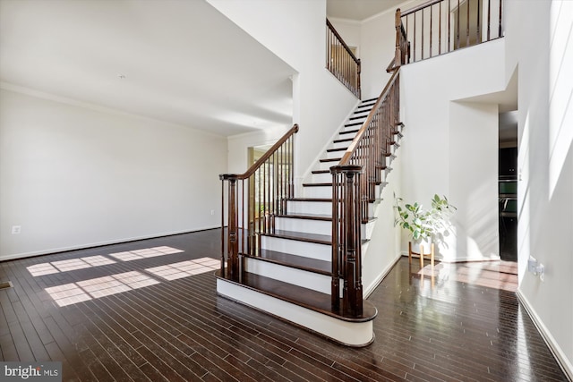 stairway featuring baseboards, a high ceiling, wood finished floors, and crown molding