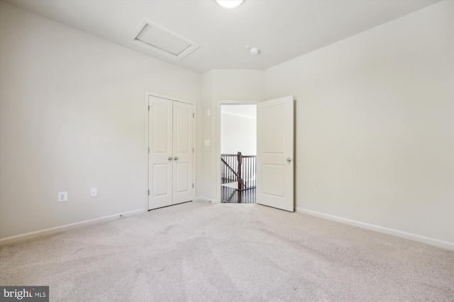 spare room with attic access, light carpet, and baseboards