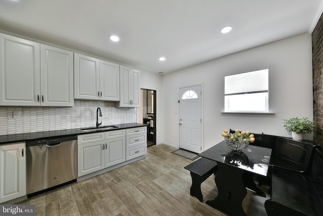 kitchen featuring stainless steel dishwasher, dark countertops, a sink, and white cabinets