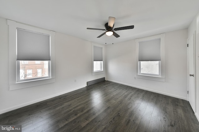 empty room featuring a baseboard heating unit, ceiling fan, baseboards, and dark wood-style floors