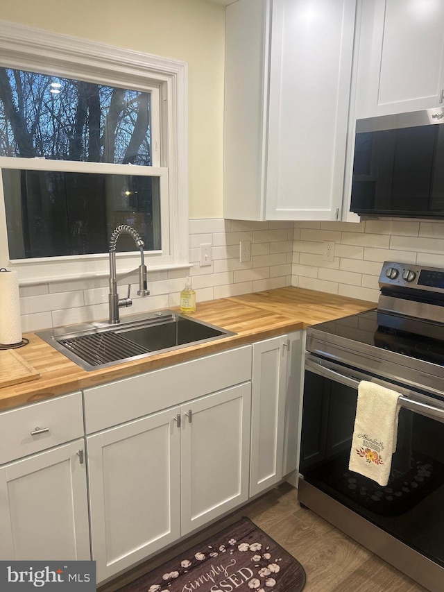 kitchen with decorative backsplash, stainless steel appliances, white cabinetry, wooden counters, and a sink