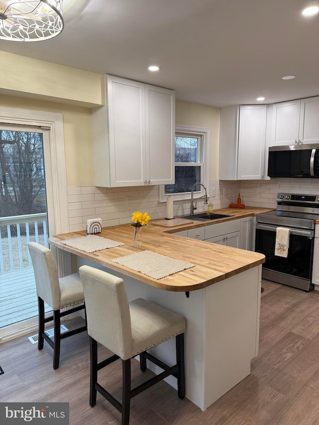 kitchen featuring a breakfast bar, butcher block counters, appliances with stainless steel finishes, white cabinets, and a peninsula