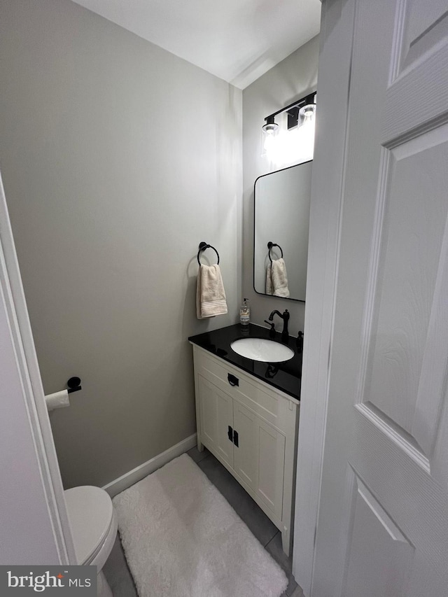 half bathroom featuring toilet, vanity, and baseboards