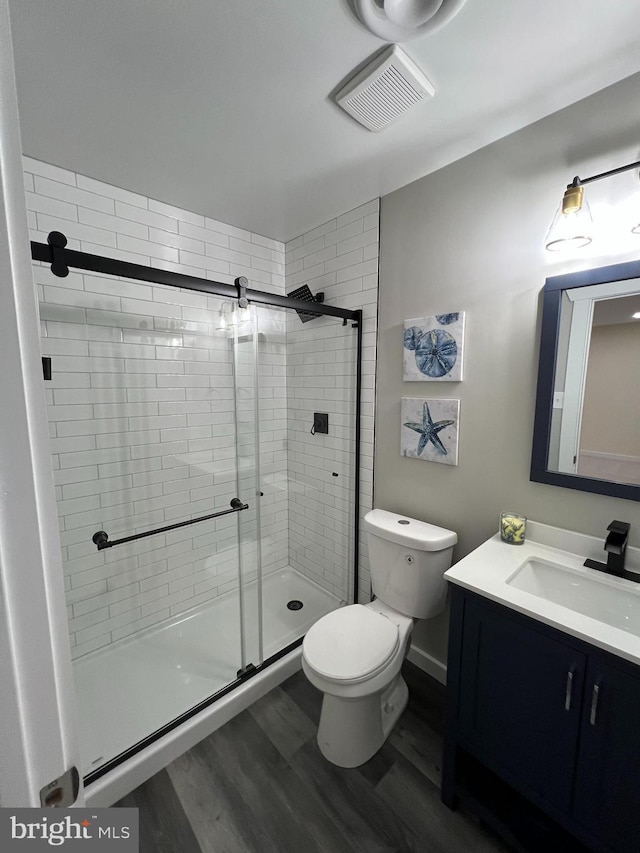 bathroom featuring a stall shower, visible vents, toilet, wood finished floors, and vanity