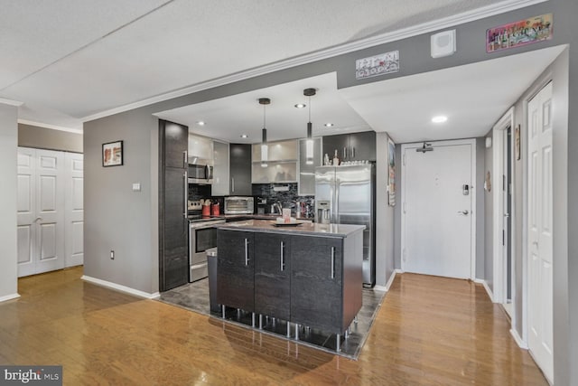 kitchen with backsplash, appliances with stainless steel finishes, ornamental molding, a kitchen island, and light wood-type flooring