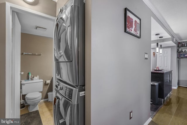 interior space with laundry area, stacked washer and dryer, wood finished floors, visible vents, and baseboards