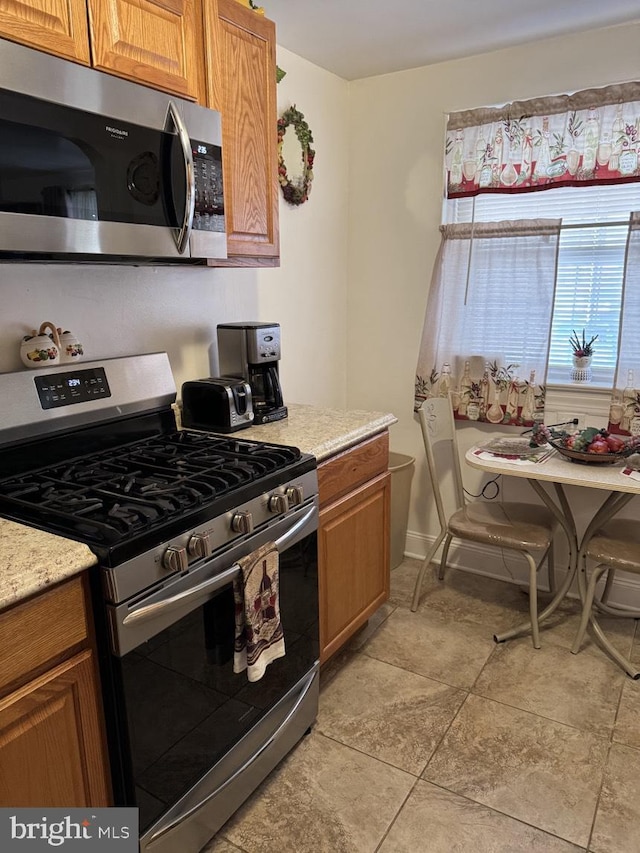 kitchen featuring stainless steel appliances, brown cabinetry, and light stone counters