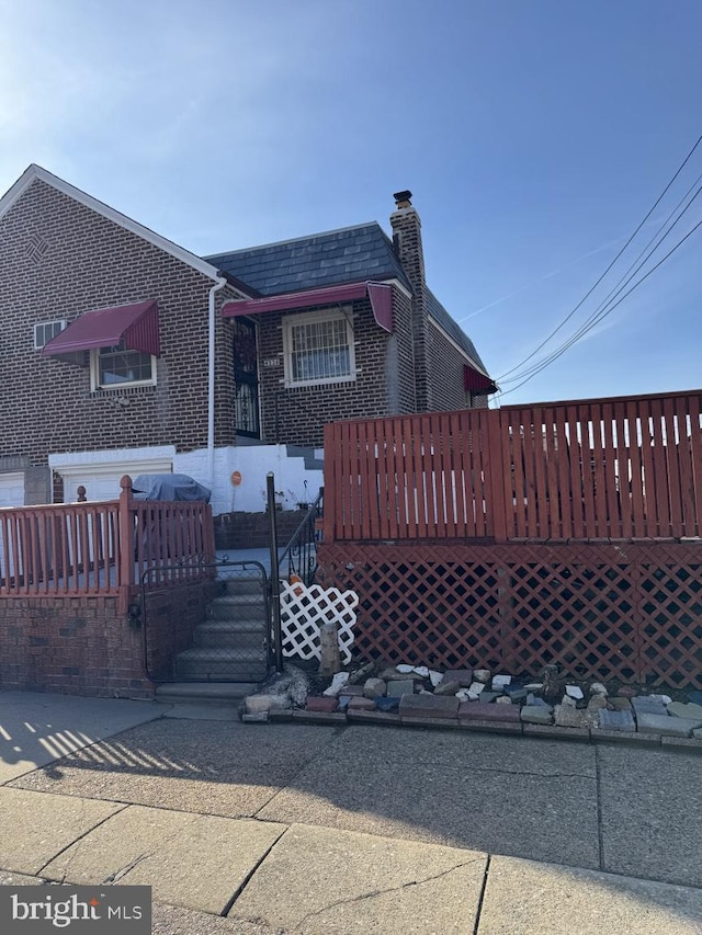 view of front of house with mansard roof, a chimney, a deck, and brick siding