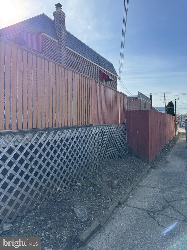 view of side of property with mansard roof, roof with shingles, and fence