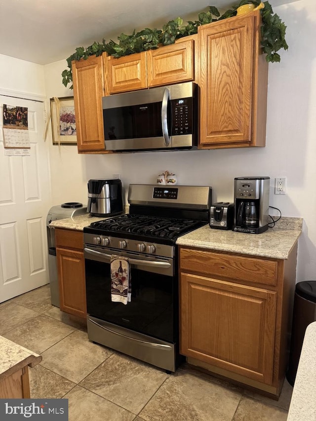 kitchen with stainless steel appliances, brown cabinetry, and light countertops