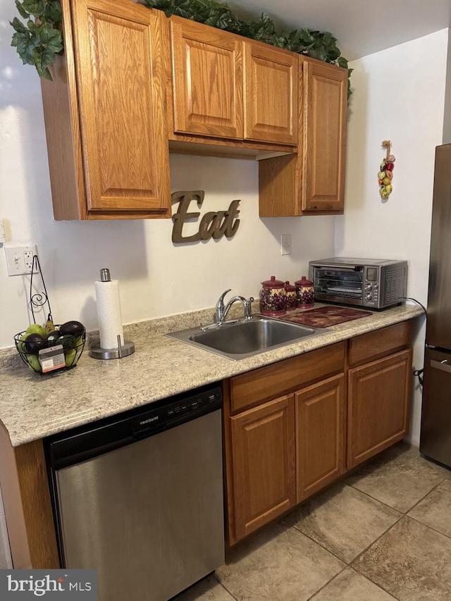 kitchen featuring a toaster, stainless steel appliances, a sink, light countertops, and brown cabinets