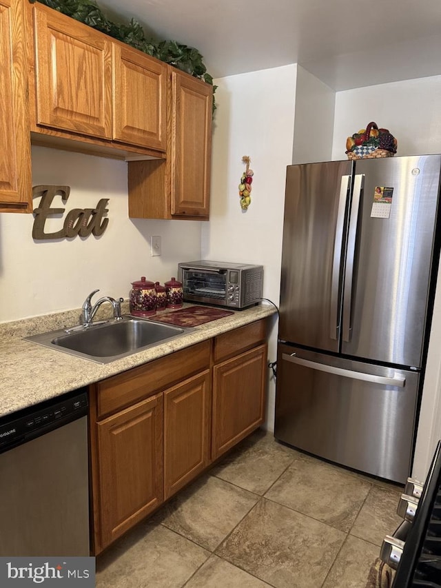 kitchen featuring light countertops, appliances with stainless steel finishes, a sink, and brown cabinets