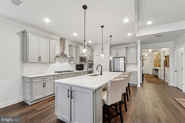 kitchen with visible vents, decorative backsplash, stainless steel appliances, wall chimney range hood, and a sink