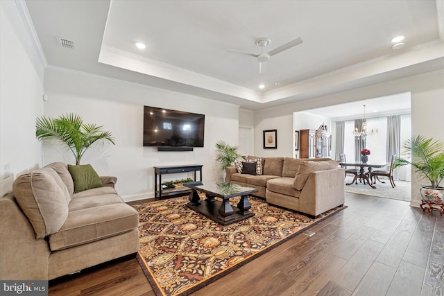 living area featuring ceiling fan with notable chandelier, dark wood-type flooring, visible vents, ornamental molding, and a raised ceiling