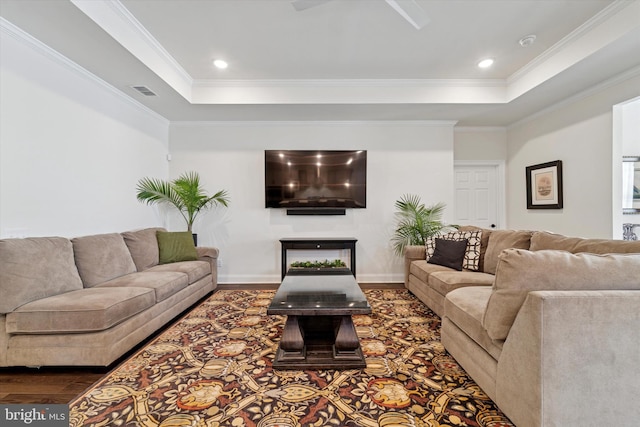 living room featuring crown molding, visible vents, a raised ceiling, and wood finished floors