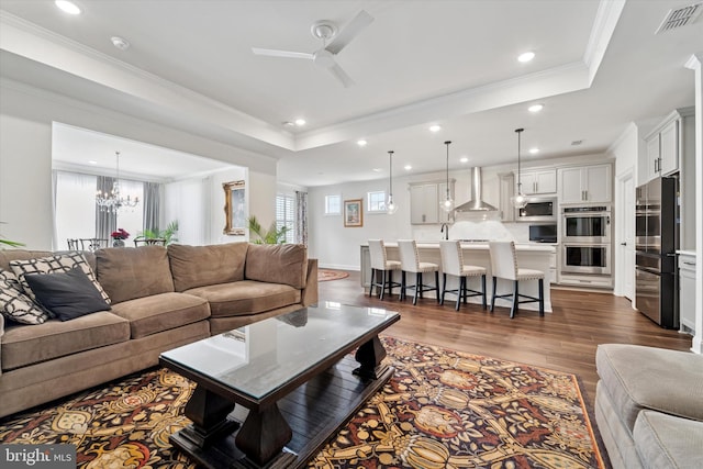 living area featuring recessed lighting, dark wood-type flooring, visible vents, a tray ceiling, and crown molding