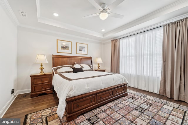 bedroom with a tray ceiling, visible vents, baseboards, and wood finished floors