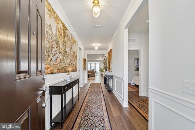 hall featuring a wainscoted wall, visible vents, crown molding, and a decorative wall