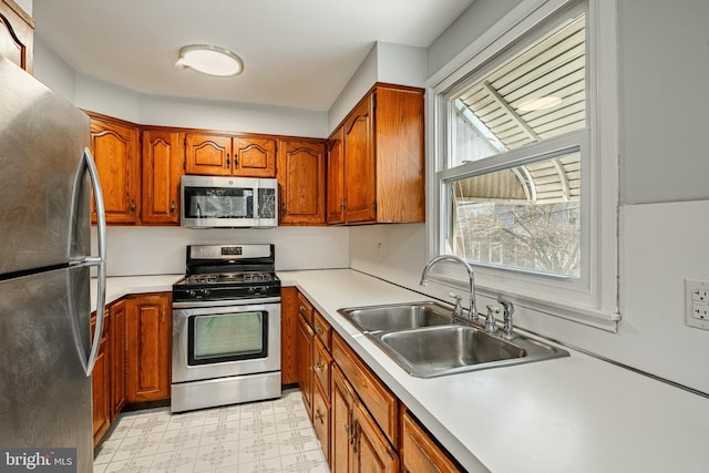 kitchen with brown cabinetry, light floors, a sink, stainless steel appliances, and light countertops