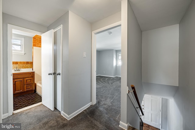 hallway featuring an upstairs landing, baseboards, a wealth of natural light, and dark colored carpet