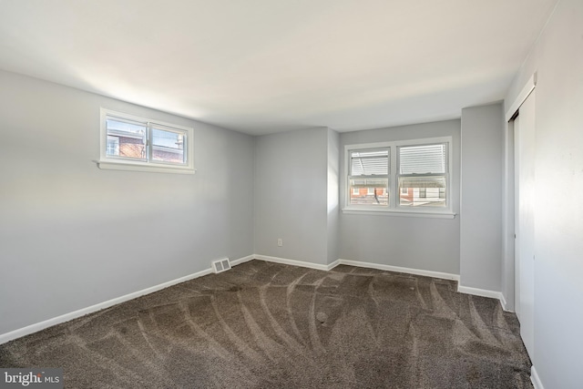 spare room with baseboards, visible vents, and dark carpet