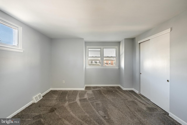 unfurnished bedroom with visible vents, baseboards, a closet, and dark carpet