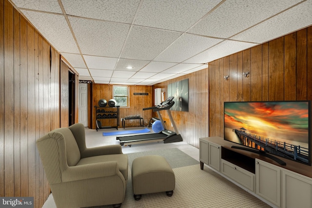 exercise room with a paneled ceiling, light carpet, and wood walls