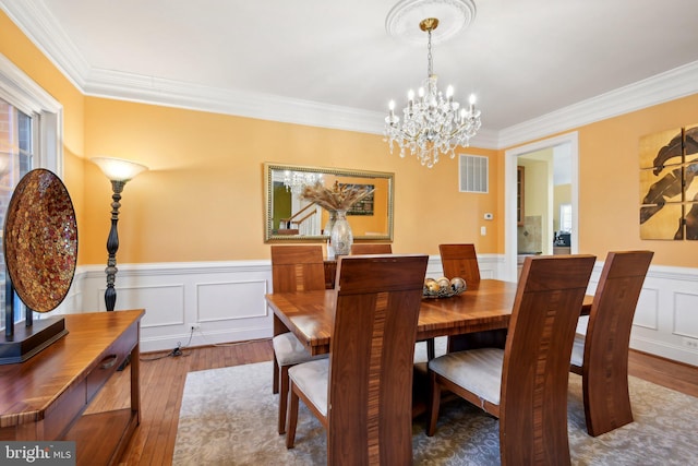 dining room with hardwood / wood-style flooring, visible vents, a wainscoted wall, and ornamental molding