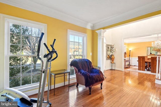 exercise area featuring baseboards, ornate columns, an inviting chandelier, crown molding, and light wood-style floors