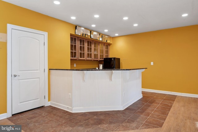 kitchen with recessed lighting, glass insert cabinets, a kitchen breakfast bar, black refrigerator, and baseboards