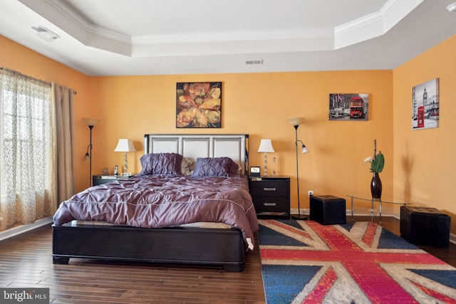 bedroom featuring a tray ceiling, wood finished floors, visible vents, and crown molding