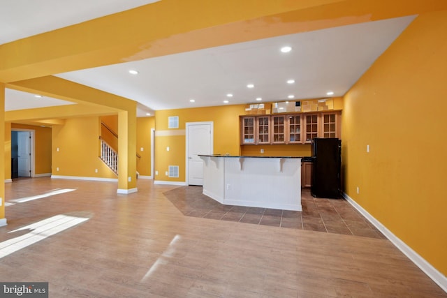 kitchen featuring visible vents, glass insert cabinets, freestanding refrigerator, an island with sink, and a kitchen bar