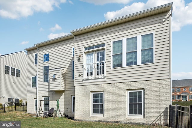 rear view of house featuring brick siding, a lawn, and fence