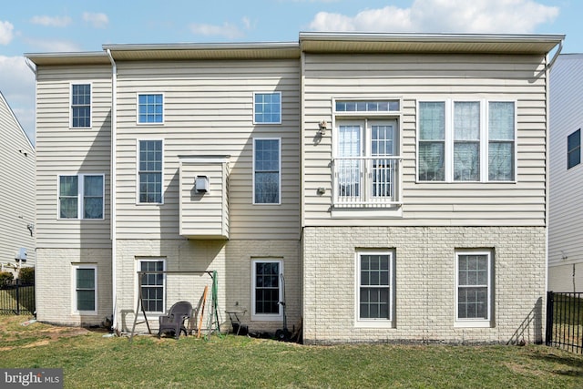 rear view of house featuring brick siding, a lawn, and fence