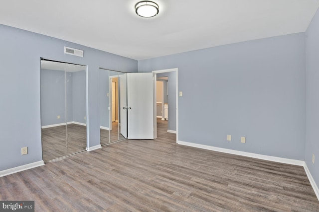 unfurnished bedroom featuring wood finished floors, visible vents, baseboards, and two closets