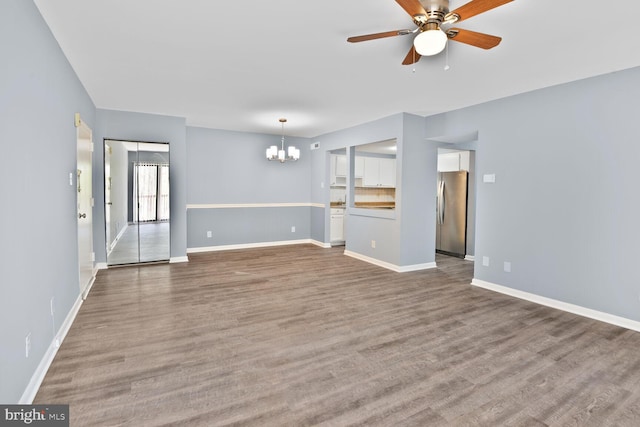 unfurnished living room featuring wood finished floors, baseboards, and ceiling fan with notable chandelier
