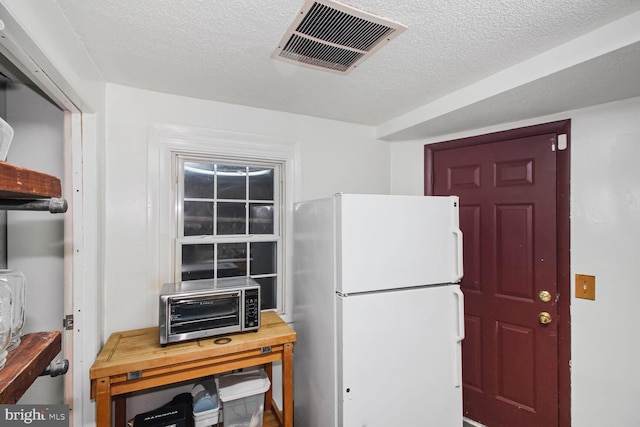 kitchen featuring freestanding refrigerator, a toaster, visible vents, and a textured ceiling