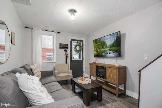 living area featuring a textured ceiling, wood finished floors, and baseboards