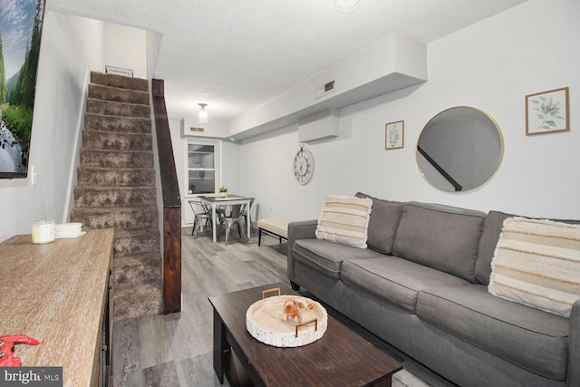 living area featuring visible vents, a textured ceiling, stairway, and wood finished floors