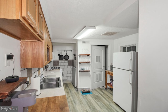 kitchen featuring light wood-style floors, freestanding refrigerator, visible vents, and a sink