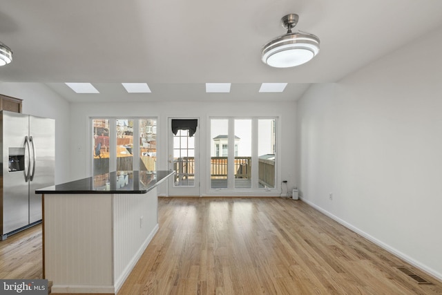 kitchen featuring light wood finished floors, visible vents, dark countertops, a center island, and stainless steel fridge