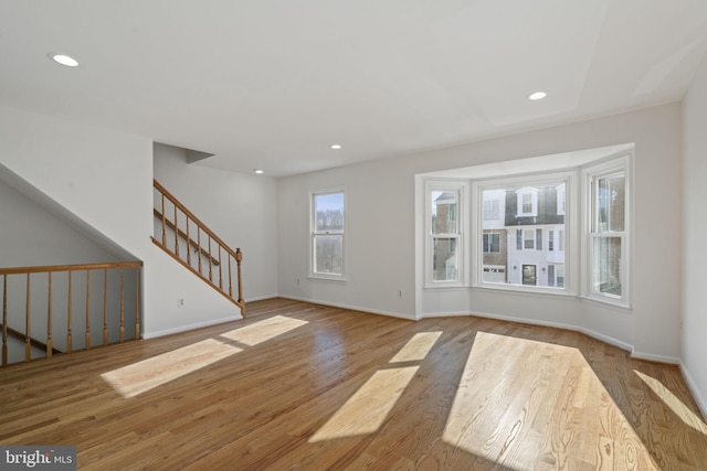 unfurnished living room with recessed lighting, baseboards, wood finished floors, and stairs